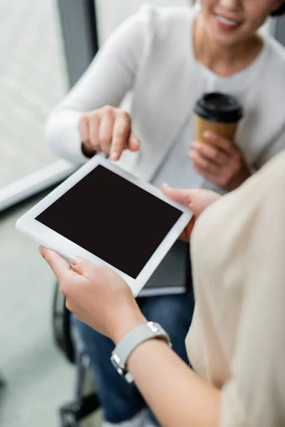 Обрізаний вид розмитої бізнес-леді з інвалідністю вказує на цифровий планшет з порожнім екраном в руках колеги — стокове фото