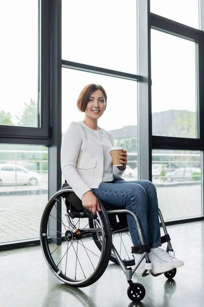 Vista completa de la mujer de negocios en silla de ruedas celebración de bebidas para llevar en la oficina - foto de stock