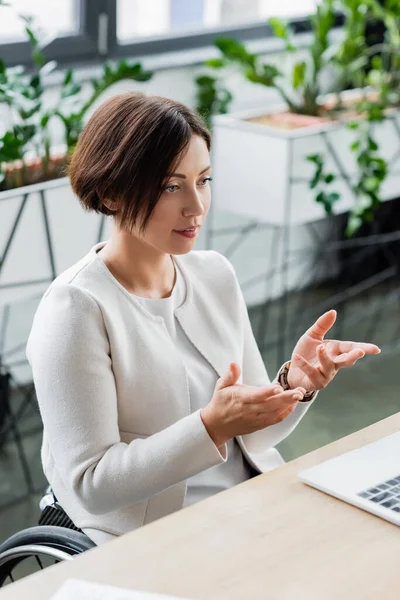 Femme d'affaires avec handicap physique pointant avec les mains lors d'un appel vidéo sur un ordinateur portable au bureau — Photo de stock