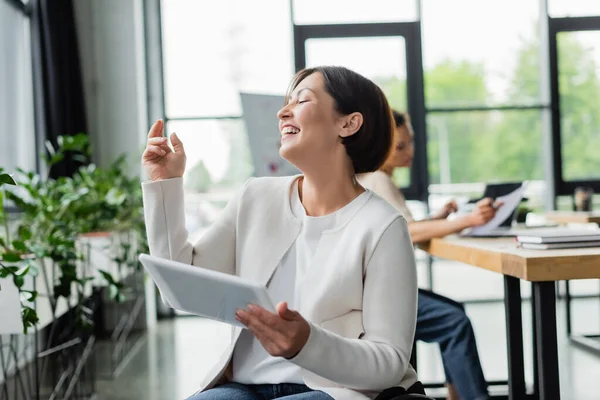 Збуджена бізнес-леді з фізичними вадами сміється, тримаючи цифровий планшет в офісі — стокове фото