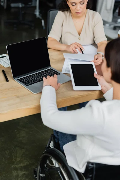 Businesswoman in wheelchair working with digital tablet and laptop near african american colleague — Stock Photo