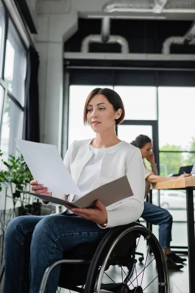 Femme d'affaires en fauteuil roulant travaillant avec des documents près floue collègue afro-américain — Photo de stock