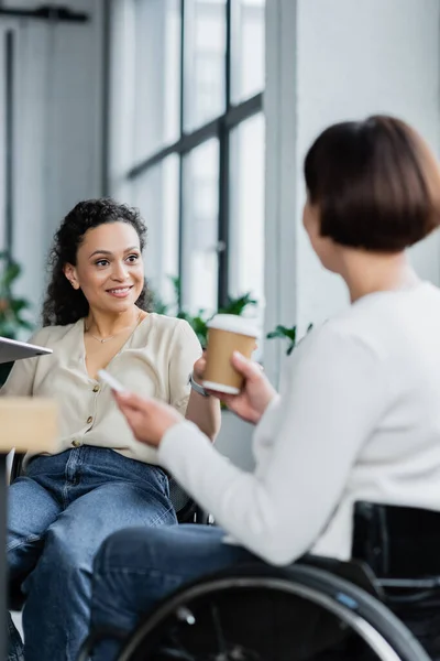 Afrikanisch-amerikanische Geschäftsfrau lächelt neben verschwommenem Kollegen im Rollstuhl — Stockfoto