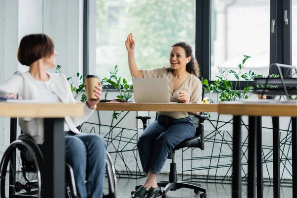 Cheerful african american businesswoman waving hand to colleague with disability on blurred foreground — Stock Photo