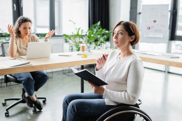 Blurred african american businesswoman gesturing at laptop near thoughtful colleague in wheelchair — Stock Photo