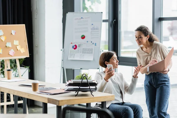 African american businesswoman and her colleague in wheelchair working near blurred flip chart with analytics — Stock Photo