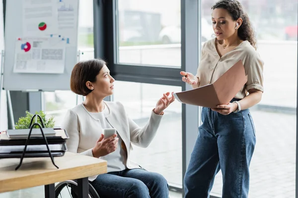 African american businesswoman and her colleague with physical disability pointing at documents during discussion — Stock Photo