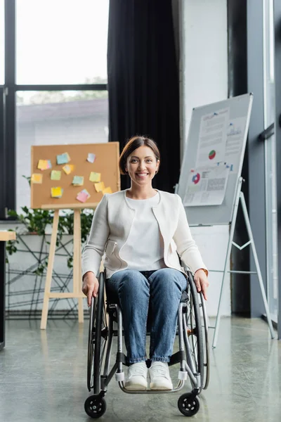 Femme d'affaires heureuse avec un handicap physique près tableau à feuilles mobiles floues et tableau de bord au bureau — Photo de stock