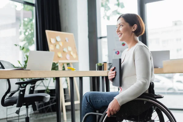 Веселая деловая женщина с ограниченными возможностями держит ноутбук на рабочем месте в офисе — стоковое фото