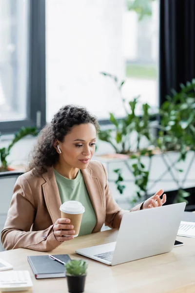 Afro-americana donna d'affari che tiene da asporto bere durante la video chat sul computer portatile in ufficio — Foto stock