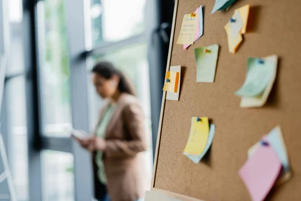 Selective focus of corkboard with sticky notes near blurred african american businesswoman in office — Stock Photo
