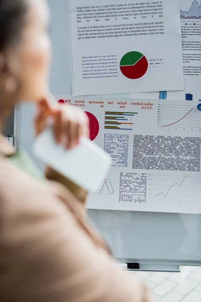 Selektiver Fokus des Flipcharts mit Infografiken in der Nähe verschwommener afrikanisch-amerikanischer Geschäftsfrau im Büro — Stockfoto