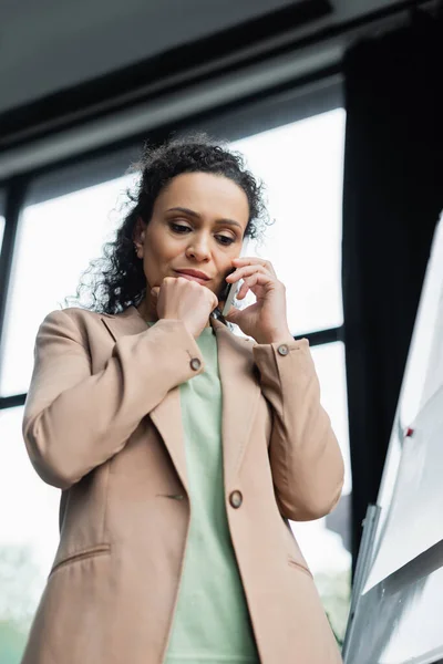 Vista de ángulo bajo de la mujer de negocios afroamericana preocupada que llama en el teléfono móvil en la oficina - foto de stock