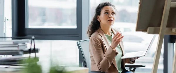 African american businesswoman with laptop pointing at note board in office, banner — Stock Photo