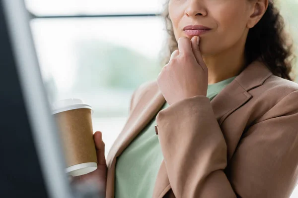 Неповний погляд на афроамериканську комерсантку, яка тримає каву, щоб піти, думаючи в офісі. — стокове фото