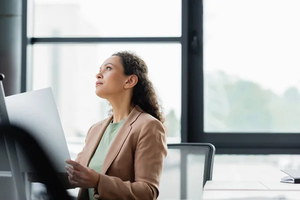 African american businesswoman holding document and looking away while thinking in office — Stock Photo