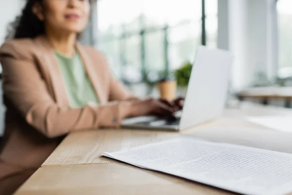 Abgeschnittene Ansicht einer verschwommenen afrikanisch-amerikanischen Geschäftsfrau, die auf dem Laptop neben Dokumenten auf dem Schreibtisch tippt — Stockfoto