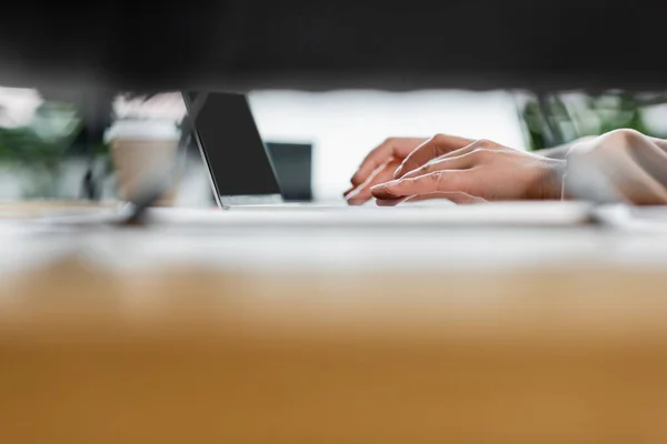 Partial view of businesswoman working on laptop with blank screen on blurred foreground — Stock Photo