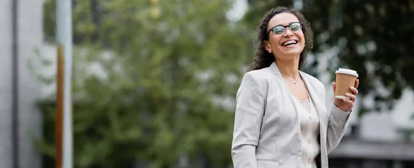 Joyeuse femme d'affaires afro-américaine souriant à la caméra tout en tenant à emporter boisson à l'extérieur, bannière — Photo de stock