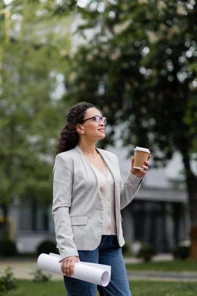 African american businesswoman with rolled documents and takeaway drink looking away outdoors — Stock Photo