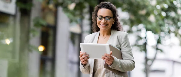 Heureuse femme d'affaires afro-américaine avec des dossiers en papier en utilisant une tablette numérique sur la rue urbaine, bannière — Photo de stock