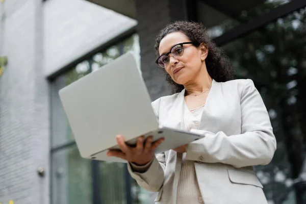 Vue à angle bas de femme d'affaires afro-américaine réfléchie regardant ordinateur portable sur la rue de la ville — Photo de stock