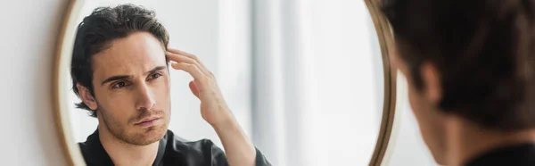 Jeune homme touchant les cheveux tout en regardant miroir dans la salle de bain, bannière — Photo de stock