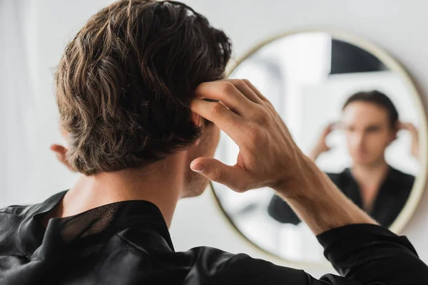Young man touching hair near blurred mirror in bathroom — Stock Photo