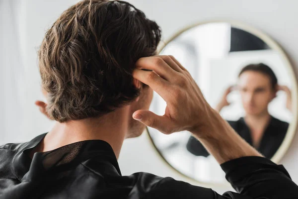 Joven tocando el pelo cerca de espejo borroso en el baño - foto de stock