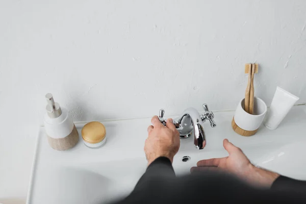 Vista recortada del hombre golpeando el agua cerca del lavabo en el baño - foto de stock