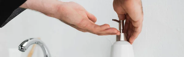 Vista recortada del hombre vertiendo jabón líquido en la mano cerca del grifo en el baño, pancarta - foto de stock