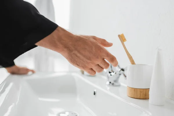 Cropped view of man pulling hand to toothbrush near sink in bathroom — Stock Photo