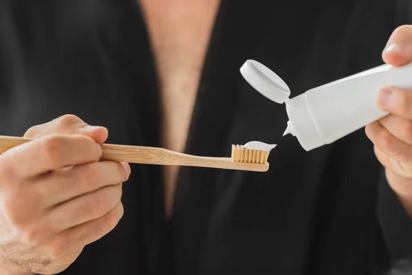 Vista recortada del hombre borroso vertiendo pasta de dientes en el cepillo de dientes - foto de stock