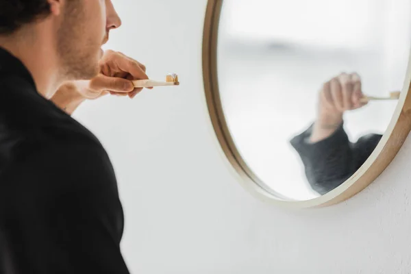 Cropped view of young man holding toothbrush near mirror in bathroom — Stock Photo