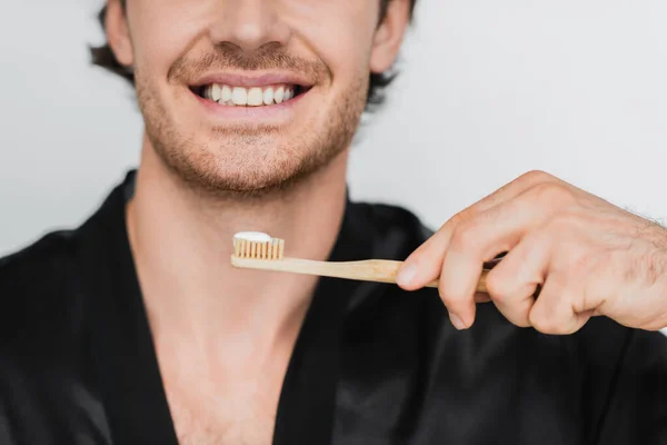 Обрезанный вид улыбающегося мужчины в халате, держащего зубную щетку изолированной на сером — стоковое фото