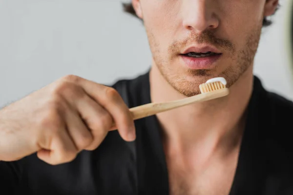 Vista ritagliata del giovane che tiene lo spazzolino da denti con dentifricio in bagno — Foto stock