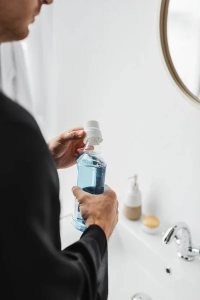 Обрезанный вид человека, держащего бутылку жидкости для полоскания рта в ванной комнате — стоковое фото