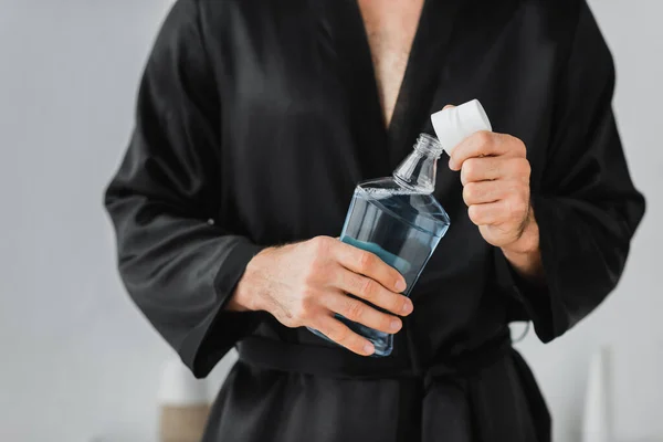 Vue recadrée de l'homme en robe de soie tenant bouteille de bain de bouche et capuchon dans la salle de bain — Photo de stock