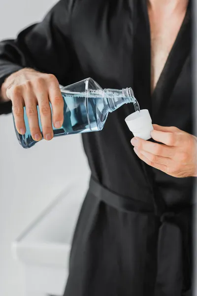 Обрезанный вид человека, наливающего жидкость для полоскания рта в крышку ванной комнаты — стоковое фото