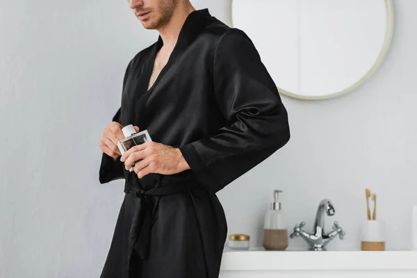 Cropped view of man in satin robe holding perfume in bathroom — Stock Photo