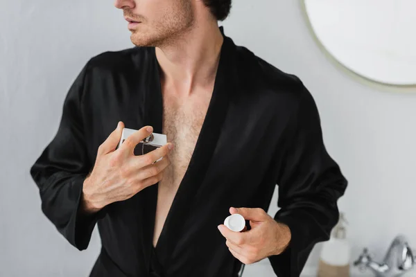 Vista cortada do homem em roupão preto aplicando perfume no banheiro — Fotografia de Stock