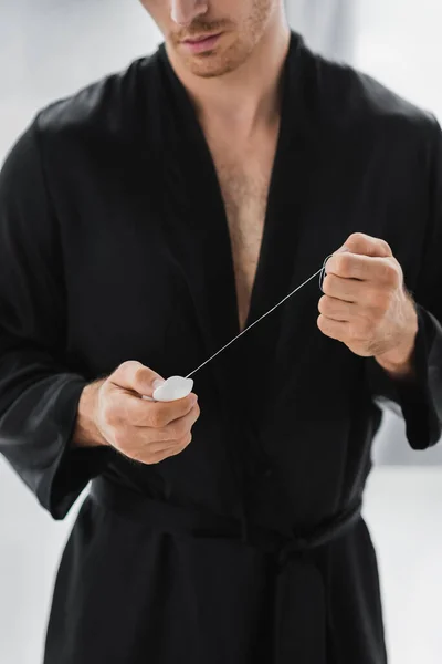 Vista cortada do homem em roupão preto segurando fio dental em casa — Fotografia de Stock