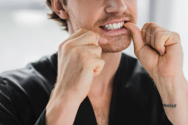 Vista recortada del hombre en bata negra limpiando los dientes con hilo dental - foto de stock