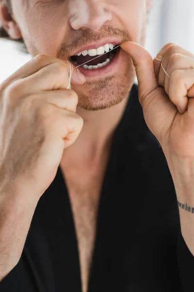 Cropped view of man in black robe cleaning teeth with dental floss — Stock Photo