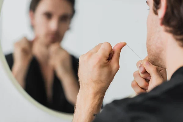 Homem desfocado segurando fio dental perto do espelho no banheiro — Fotografia de Stock