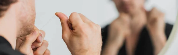 Cropped view of man holding dental floss near blurred mirror in bathroom, banner — Stock Photo