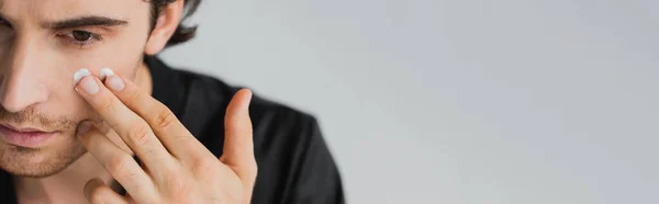 Cropped view of young man in robe applying cosmetic cream on face isolated on grey, banner — Stock Photo