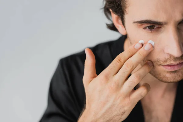 Cropped view of young man applying cream on face isolated on grey — Stock Photo