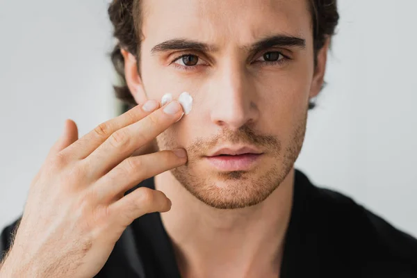 Joven mirando a la cámara mientras aplica crema cosmética - foto de stock