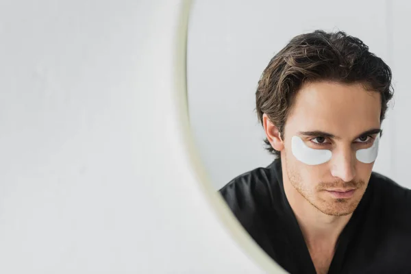 Jeune homme avec des yeux patchs regarder miroir dans la salle de bain — Photo de stock